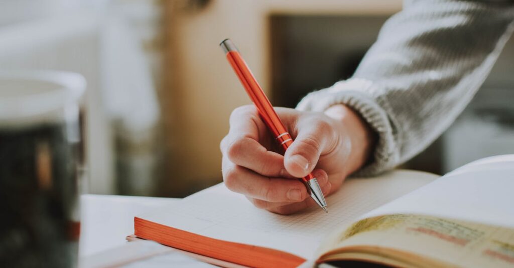 A person writing in a notebook with a red ballpoint pen, showcasing detail and focus.
